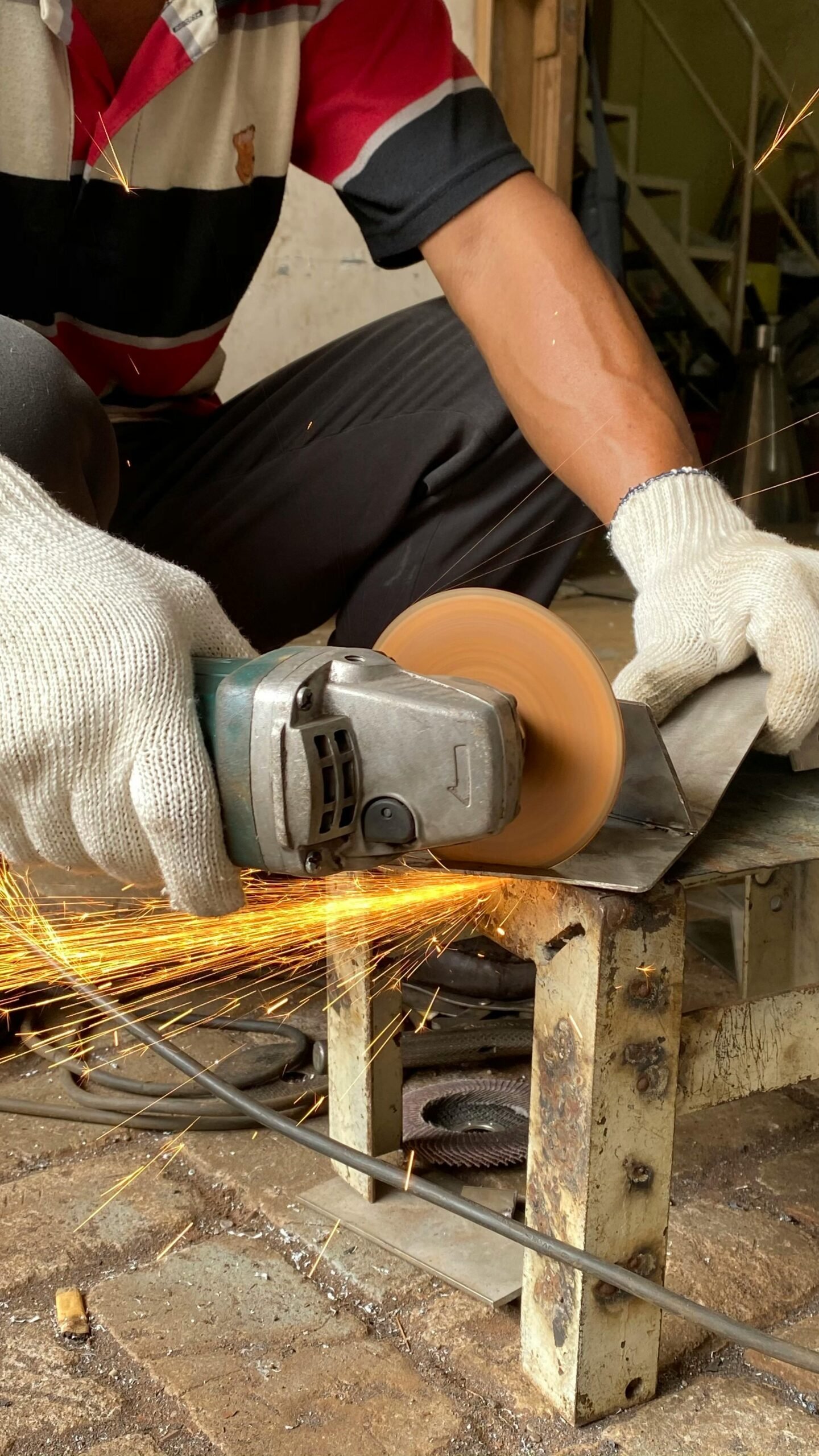 A metalworker skillfully uses a grinder, creating sparks in an industrial workshop setting.